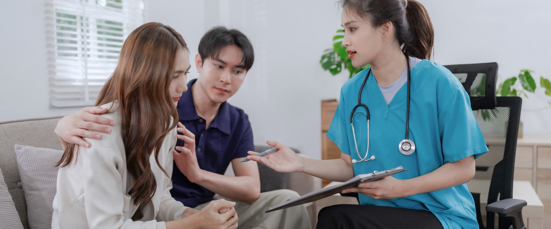 A healthcare provider in scrubs speaking with a couple, explaining something while holding a clipboard