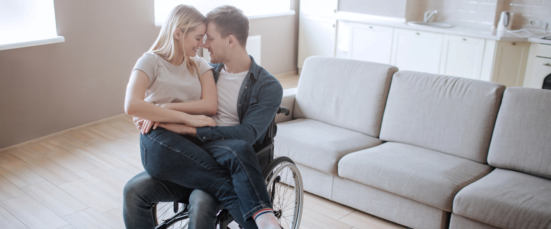 A couple sharing an intimate moment - a woman sitting in the lap of a man in a wheelchair, foreheads touching