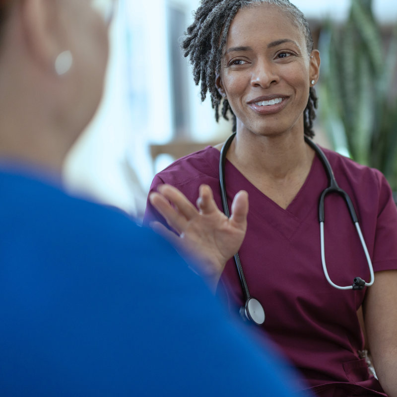 Healthcare provider in scrubs with stethoscope having a warm conversation with a colleague