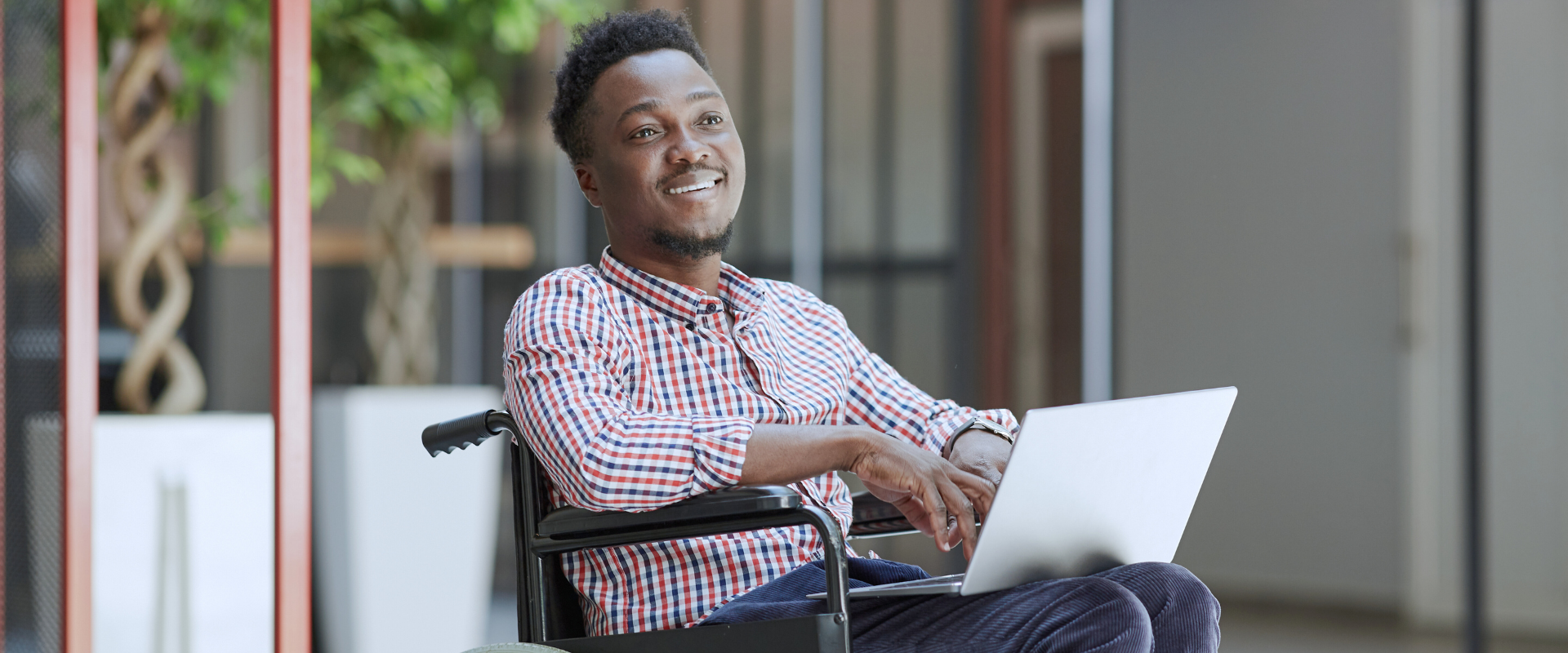 A smiling man in a wheelchair using a laptop outdoors