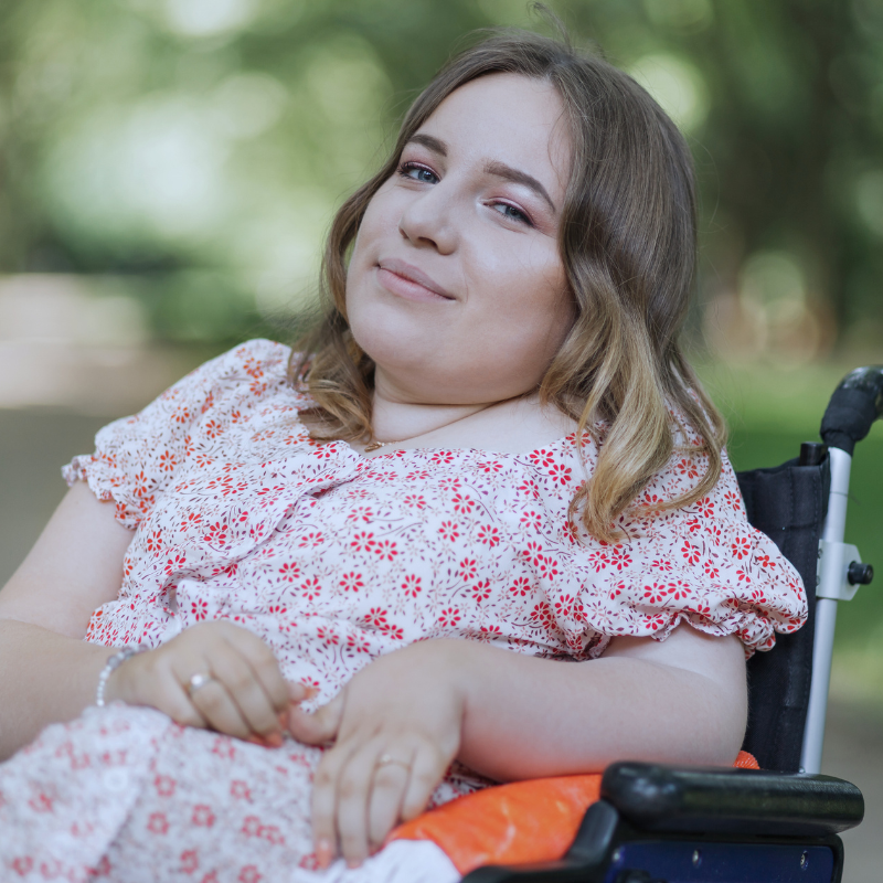 A young woman in a wheelchair smiling peacefully outdoors